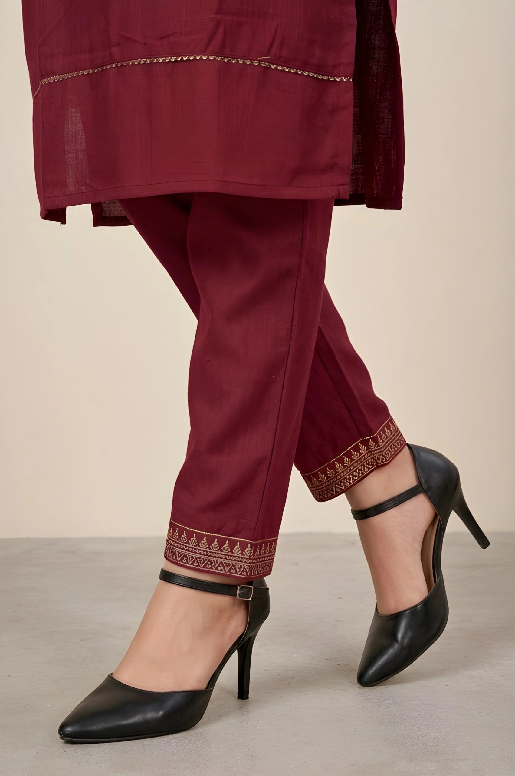 Maroon traditional outfit with embroidered pants and black high-heeled shoes on a neutral background
